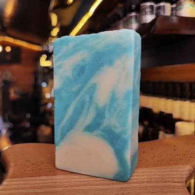 Sabonete azul e branco marmoreado sobre madeira com prateleiras e frascos ao fundo