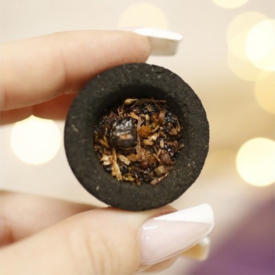 Mão segurando recipiente preto com conteúdo granulado castanho