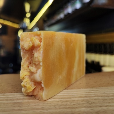 Queijo amarelo alaranjado com textura firme sobre superfície de madeira