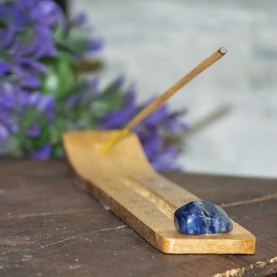 Suporte de incenso em madeira com pedra azul polida e flores roxas ao fundo