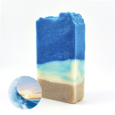 Sabonete artesanal em barras coloridas azul, branco e bege com textura lisa e detalhe inferior com superfície irregular.