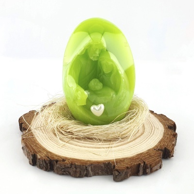 Ovo verde translúcido com relevo de família e coração branco sobre base de madeira