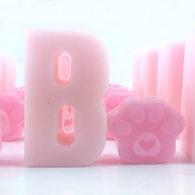 Letra B rosa translúcida e pata de animal rosa translúcida sobre superfície branca.