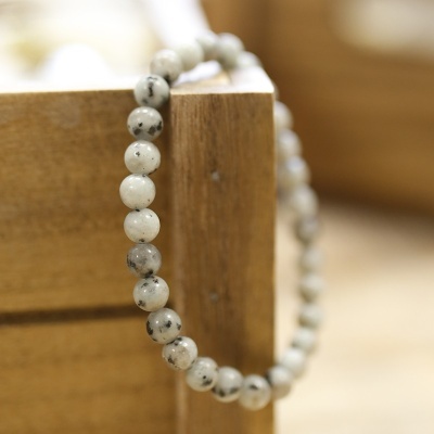 Pulseira de contas brancas com manchas pretas pendurada numa caixa de madeira clara