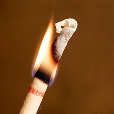 Pavio branco com faixas preta e vermelha aceso, fundo castanho desfocado