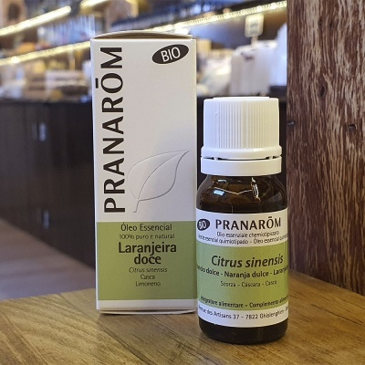 Frasco pequeno de óleo essencial PRANARÔM Laranjeira doce em embalagem branca e verde sobre mesa de madeira