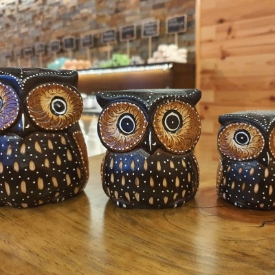 Três estatuetas de coruja em madeira decorativa em diferentes tamanhos sobre mesa de madeira