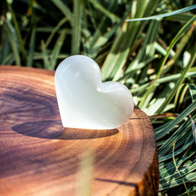 Coração de pedra branca translúcida sobre base de madeira com relva ao fundo