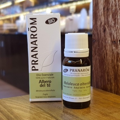 Frasco de óleo essencial Pranarôm Melaleuca alternifolia ao lado da embalagem sobre mesa de madeira.