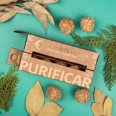 Caixa de bombas herbais e quatro bombas redondas castanhas em fundo verde com folhas secas e verdes