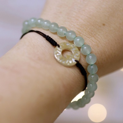 Pulseira dupla com contas verdes e pingente circular bege em cordão preto no pulso