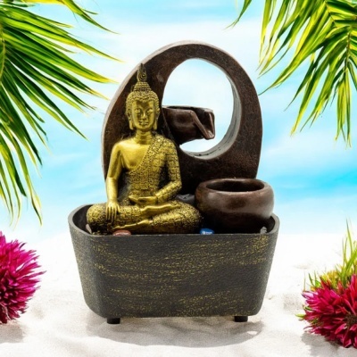Fonte de água decorativa com Buda dourado e base castanha em areia branca com plantas tropicais
