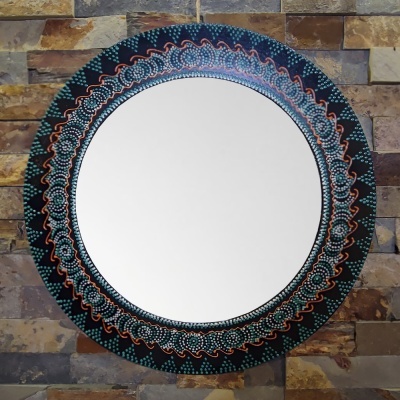 Espelho redondo com moldura decorativa em padrões geométricos coloridos numa parede de pedra.