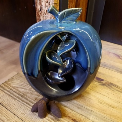 Escultura cerâmica azul e preta em forma de maçã com folhas no topo