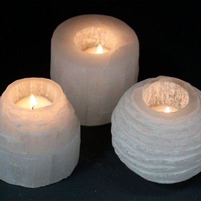 Três castiçais de selenite com velas acesas sobre fundo preto