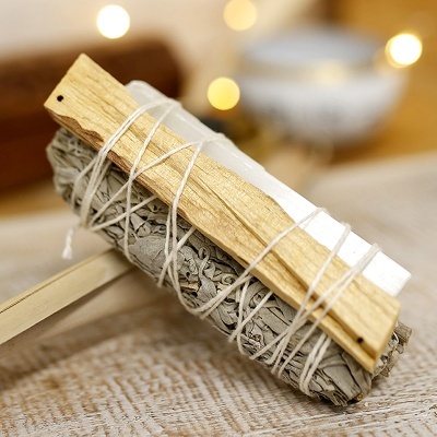 Conjunto de sálvia branca, pau santo e cristal amarrados com cordão branco sobre mesa de madeira.