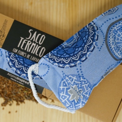 Saco térmico azul com padrão circular e etiqueta preta junto a embalagem castanha e flores secas