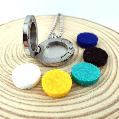 Medalhão metálico cromado aberto com cinco discos de feltro coloridos sobre superfície de madeira