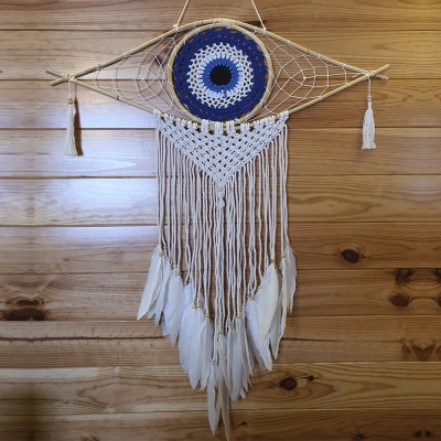 Apanhador de sonhos em forma de olho com fios trançados e penas brancas suspenso numa parede de madeira clara