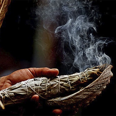 Feixe de ervas secas fumegante segurado por uma mão sobre uma concha