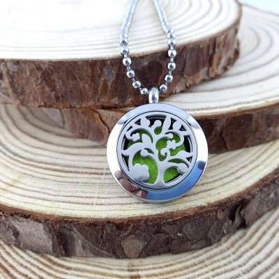 Colar prateado com pendente redondo com padrão de árvore e fundo verde sobre troncos de madeira