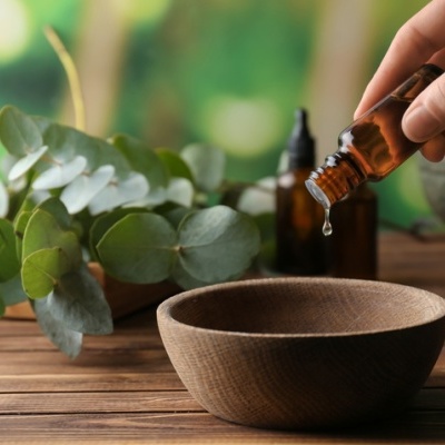 Gotas a cair de um frasco âmbar para uma tigela de madeira com folhas verdes ao fundo