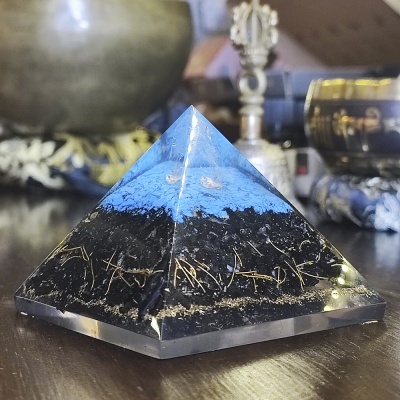 Pirâmide decorativa azul, preta e dourada sobre mesa de madeira