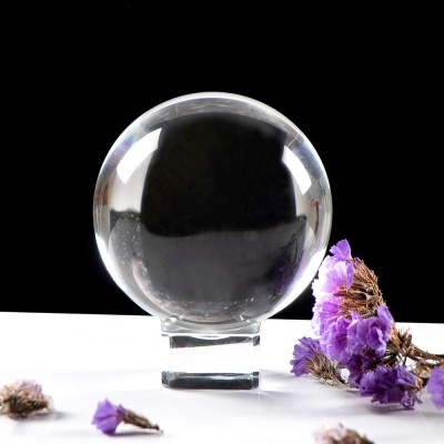 Esfera de cristal transparente com flores secas roxas ao lado sobre superfície branca.