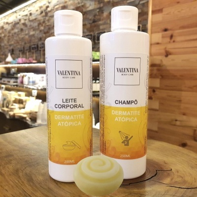 Dois frascos de produto corporal Valentina para dermatite atópica com um sabonete redondo na frente