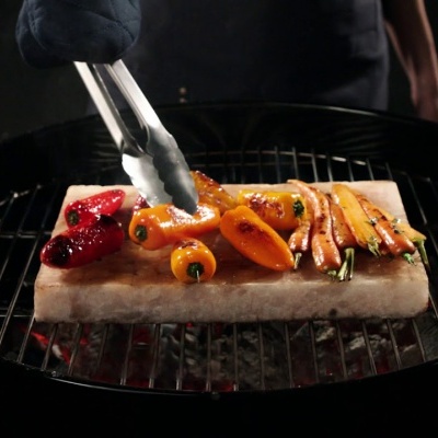 Grelhador com legumes coloridos a serem grelhados numa pedra de sal retangular.