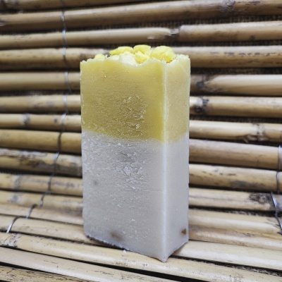 Sabonete amarelo e branco com decoração de flor sobre fundo de ripas de madeira