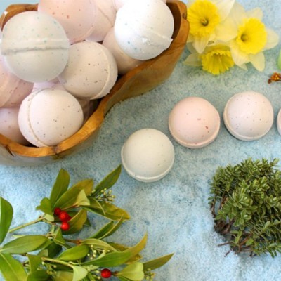 Bolas de banho brancas e cor de rosa com manchas, tigela de madeira, flores amarelas e folhas verdes com bagas sobre toalha azul