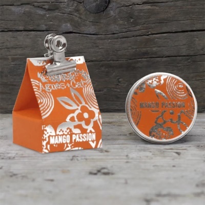 Embalagem laranja e recipiente redondo do produto Mango Passion com detalhes prateados