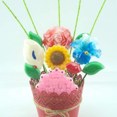 Arranjo decorativo com flores artificiais coloridas num vaso metálico vermelho com laço de corda