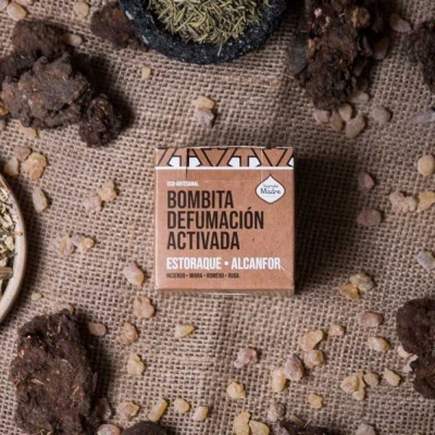 Embalagem quadrada de papel reciclado para defumação ativa, em tecido de juta, rodeada por pedras e resina.