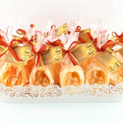 Produtos de confeitaria embalados com fitas vermelhas e etiquetas douradas numa bandeja branca rendilhada