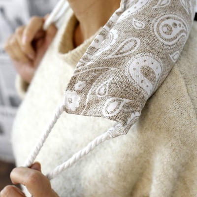 Máscara facial de tecido bege com padrão paisley e cordões brancos