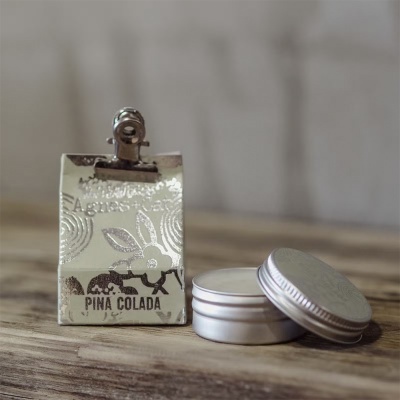 Produto cosmético Pina Colada com embalagem metálica floral e frasco redondo prateado