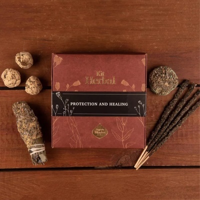 Kit herbal com caixa castanha, incensos, bolas e maço de ervas sobre mesa de madeira.