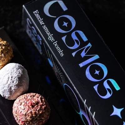 Caixa de cosméticos preta com texto azul e três bolas coloridas em superfície escura