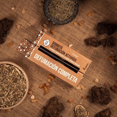 Caixa de papelão com texto 'BOMBITA DEFUMACIÓN ACTIVADA' e ervas secas sobre juta