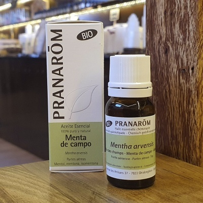 Frasco e caixa de aceite esencial de menta de campo Pranarôm sobre mesa de madeira