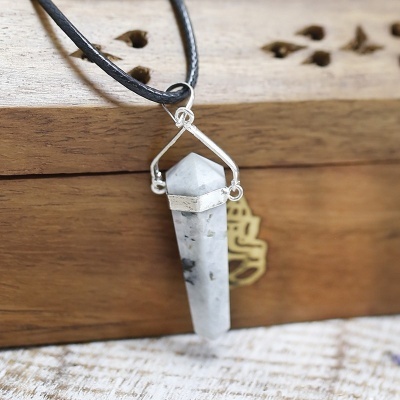 Colar com pendente de pedra branca e estrutura metálica sobre caixa de madeira