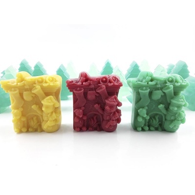 Três velas coloridas decorativas com detalhes em relevo, em amarelo, vermelho e verde claro, com pinheiros verdes ao fundo