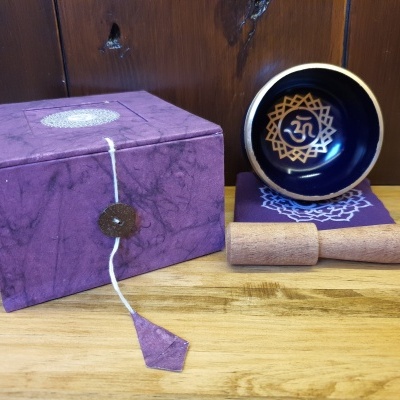 Taça de canto azul com símbolo OM dourado, bastão de madeira, base roxa com padrão branco e caixa roxa texturizada