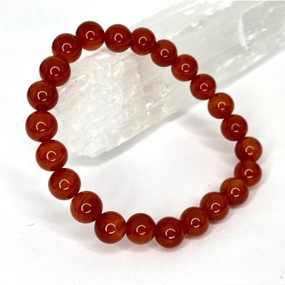 Pulseira de contas vermelhas polidas sobre base branca translúcida