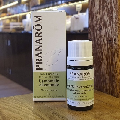 Frasco e caixa de óleo essencial Pranarôm Camomila alemã sobre mesa de madeira