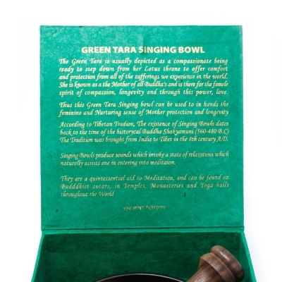 Caixa verde aberta com texto em inglês explicando 'GREEN TARA SINGING BOWL', interior em veludo, com tigela de canto tibetana e malhete de madeira.