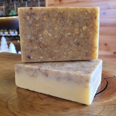 Duas barras de sabão artesanal bege com aveia sobre tabela de madeira