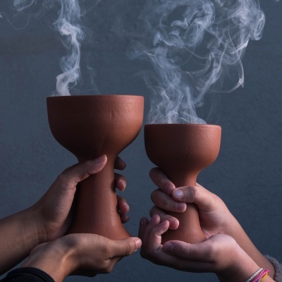Recipientes de cerâmica terracota com fumo branco sendo segurados por mãos
